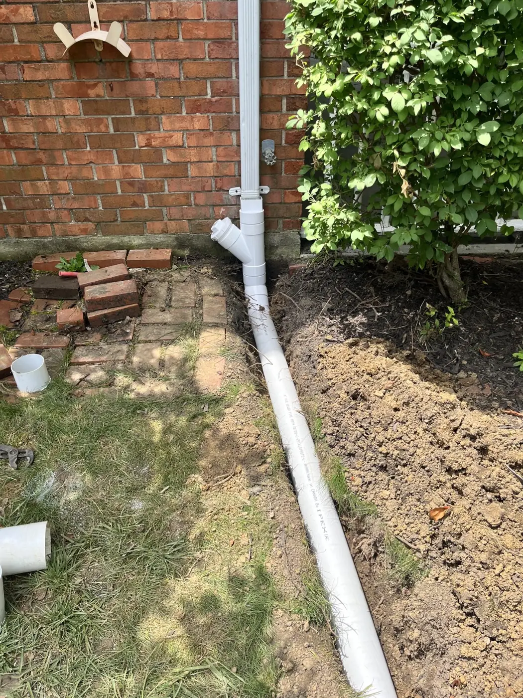 Downspout connected to a solid underground drain with a cleanout access beside a Miami Valley home
