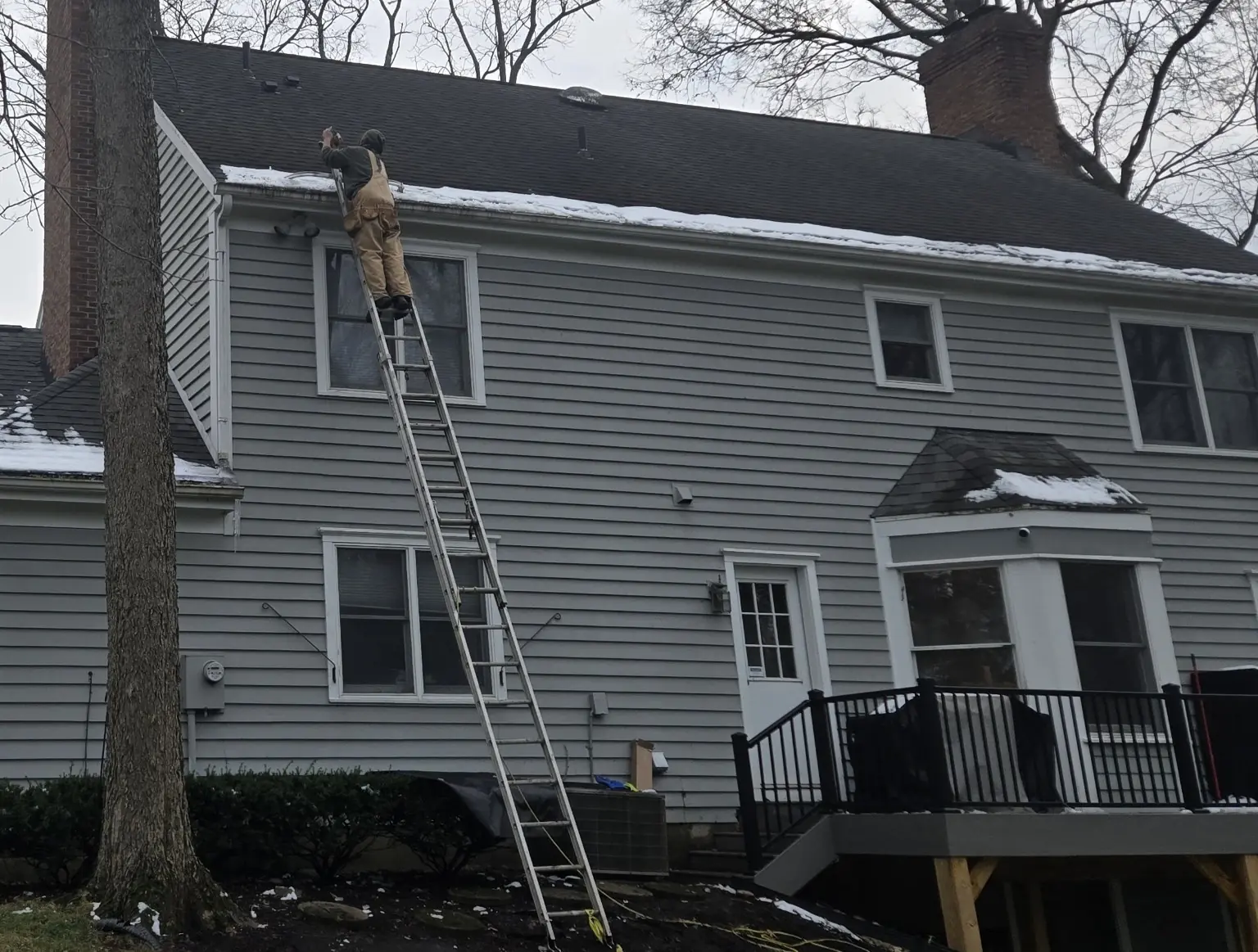 CleanFlow crew member working from a ladder at the gutter line during snowy conditions